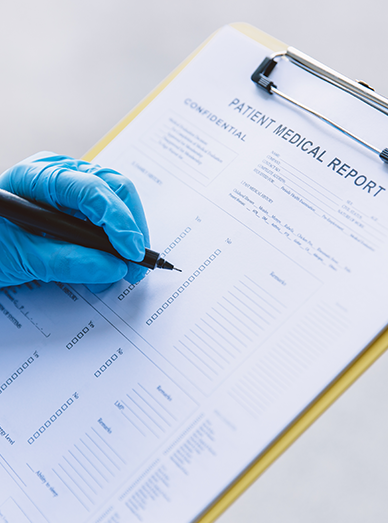 Close-up of a gloved hand filling out a patient medical report form at Mittagong Doctors.